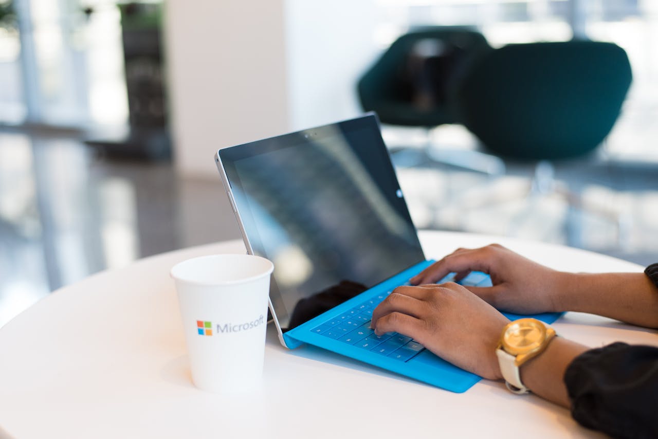 why-choose-us Hands typing on a blue keyboard with a branded cup on a table.