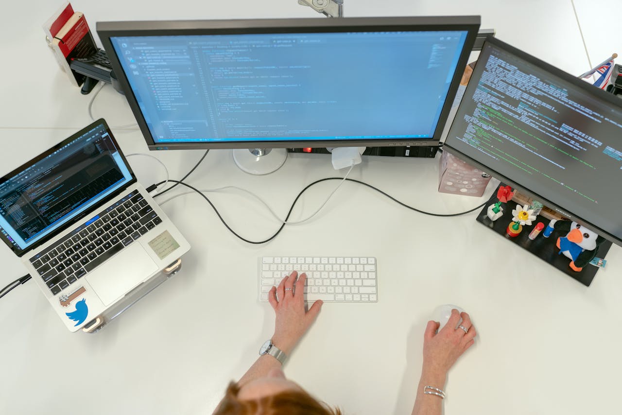 about-01 A female software engineer coding on dual monitors and a laptop in an office setting.