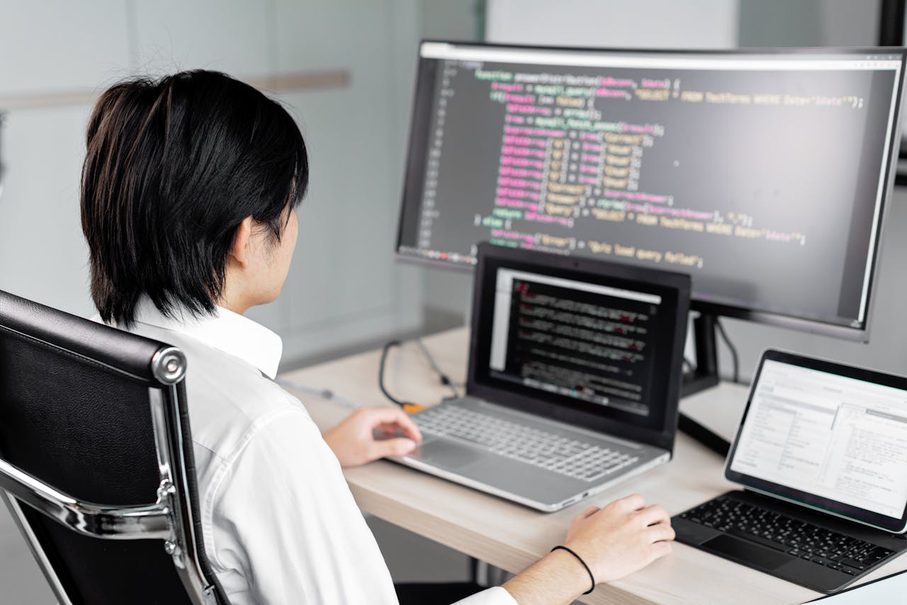 hero-img-02 A software developer working on code with multiple screens in a modern office setting.